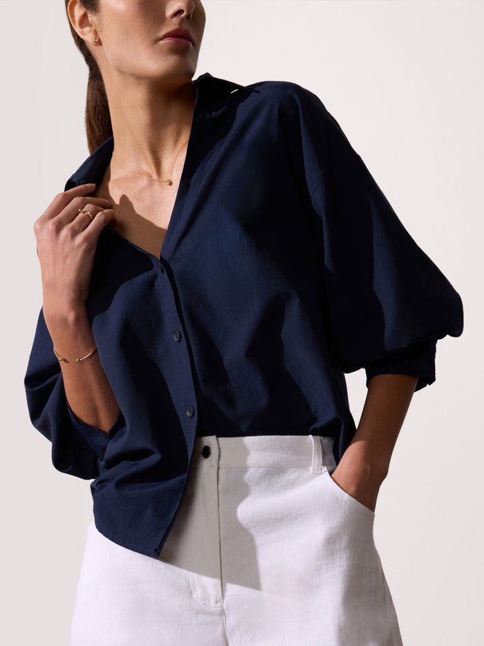 Woman wearing a navy button-up shirt with balloon sleeves and white trousers