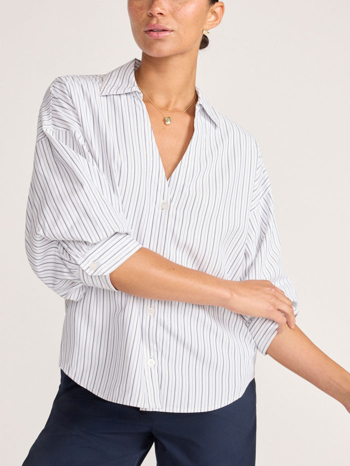 Front view of a model wearing an oversized navy striped shirt with rolled sleeves over navy trousers