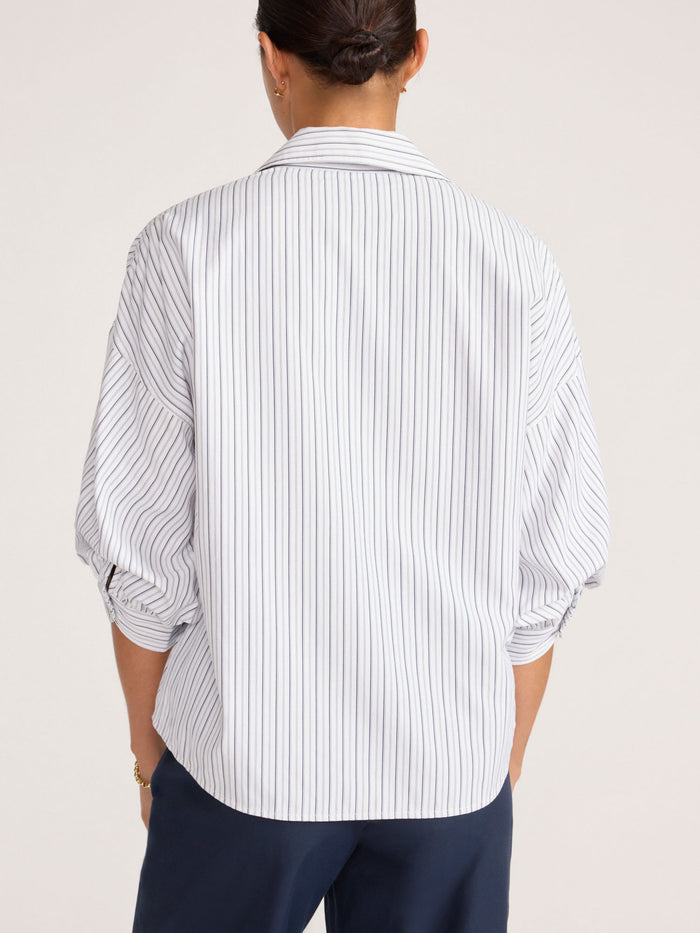 Back view of a model wearing an oversized navy striped shirt tucked into navy trousers