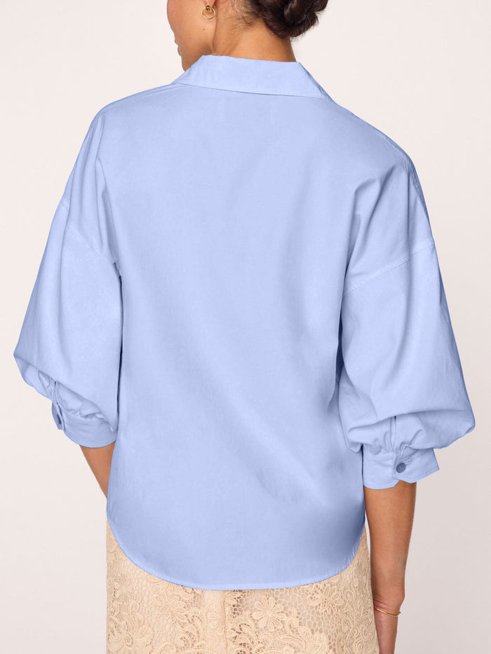 Back view of a light blue button-front blouse with balloon sleeves, worn by a model