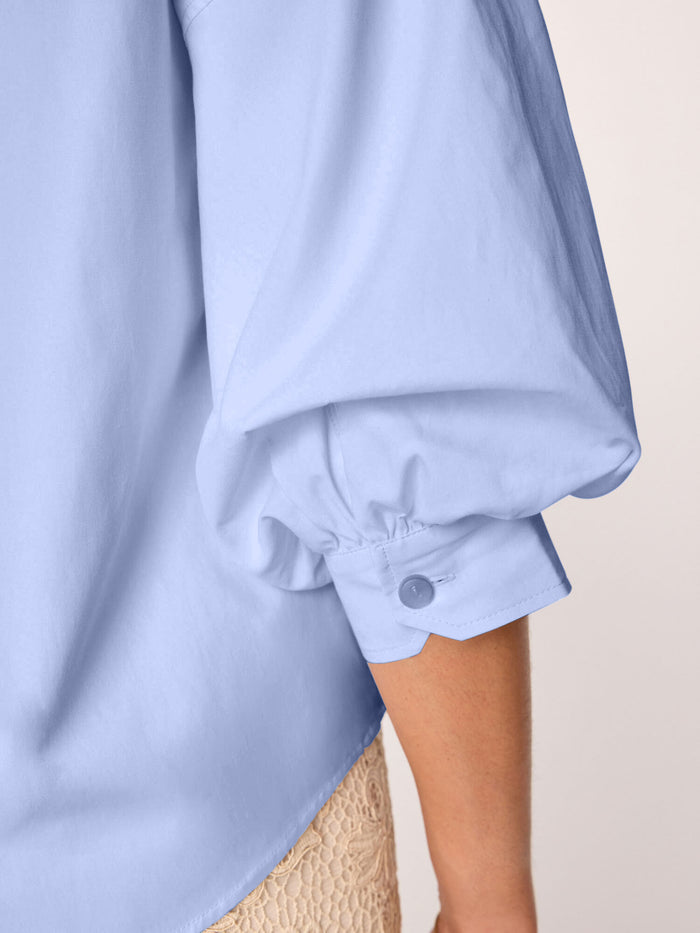 Close-up of a light blue blouse sleeve cuff with a button detail