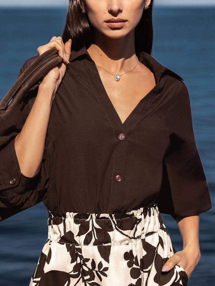 Woman wearing a brown collared blouse with a brown and cream floral print skirt against an ocean backdrop