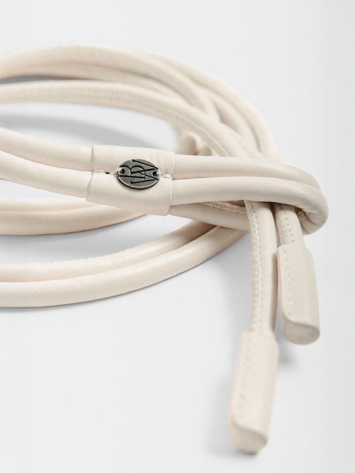 Close-up of a coiled cream leather belt showing logo hardware and tasseled ends