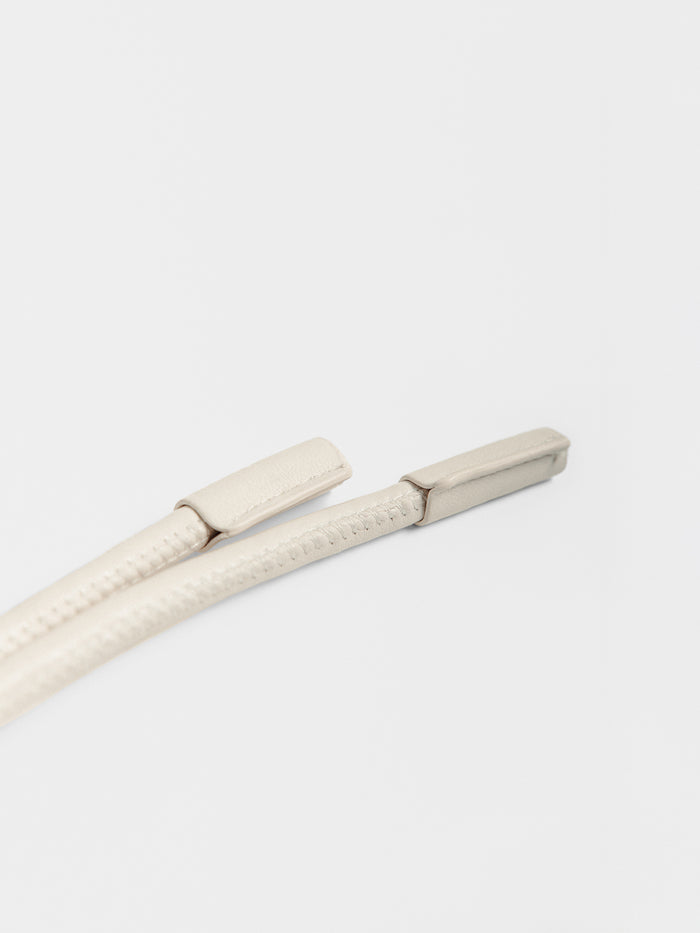 Close-up of ivory leather cord belt ends resting side by side