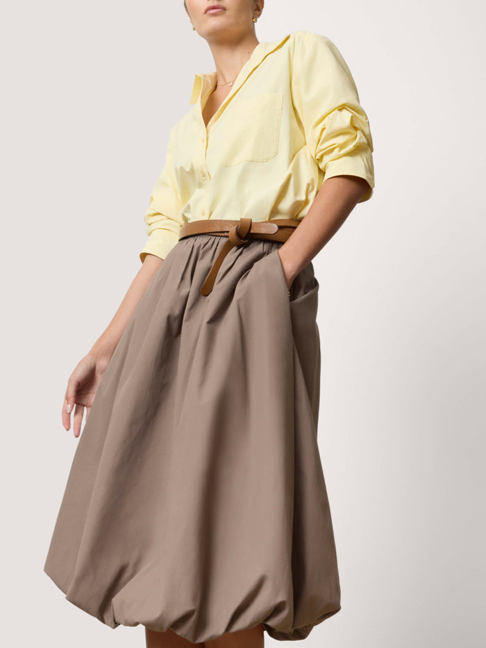 Woman wearing a pale yellow blouse with a belted brown bubble midi skirt