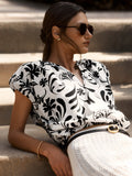 Woman sitting on outdoor steps wearing the Loui Printed Shirt in a black-and-white floral Estara print