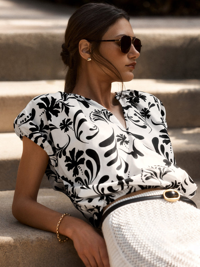 Woman sitting on outdoor steps wearing the Loui Printed Shirt in a black-and-white floral Estara print