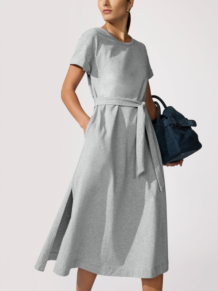 Woman wearing a grey heathered T-shirt dress with a tie waist, carrying a navy bag
