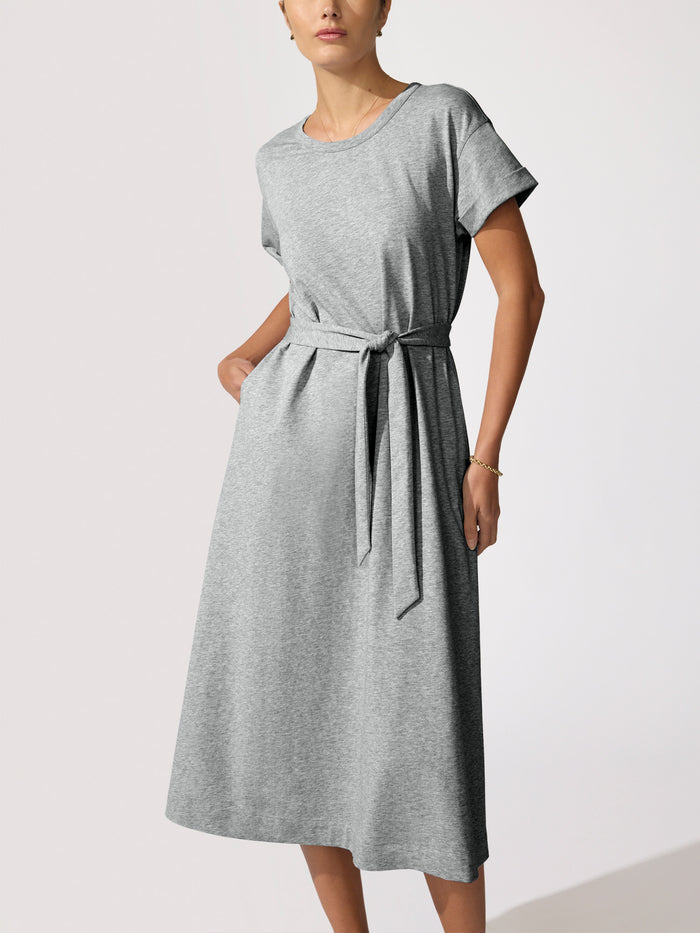 Front view of a woman wearing a grey heathered T-shirt dress with a tie waist, hand in pocket
