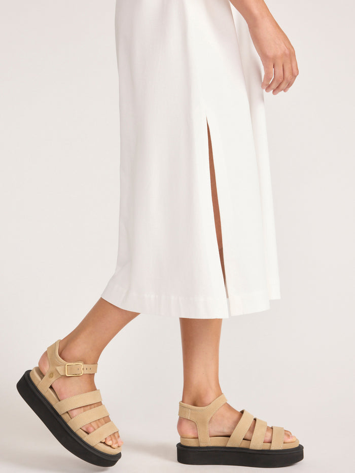 Detail of an ivory Marah dress with a side slit hem, worn with tan platform sandals.