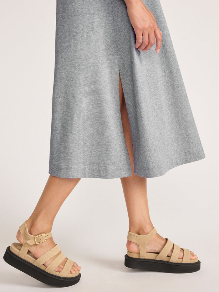 Close-up of the grey heathered T-shirt dress hem with a side slit, paired with tan platform sandals