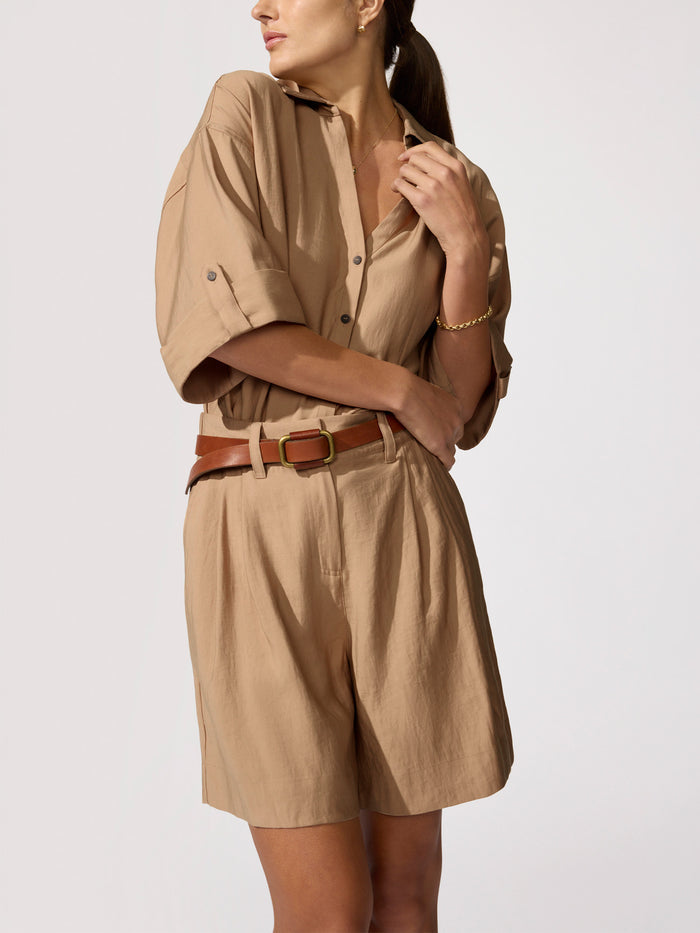 Woman wearing a tan shirt and shorts set cinched with a brown leather belt