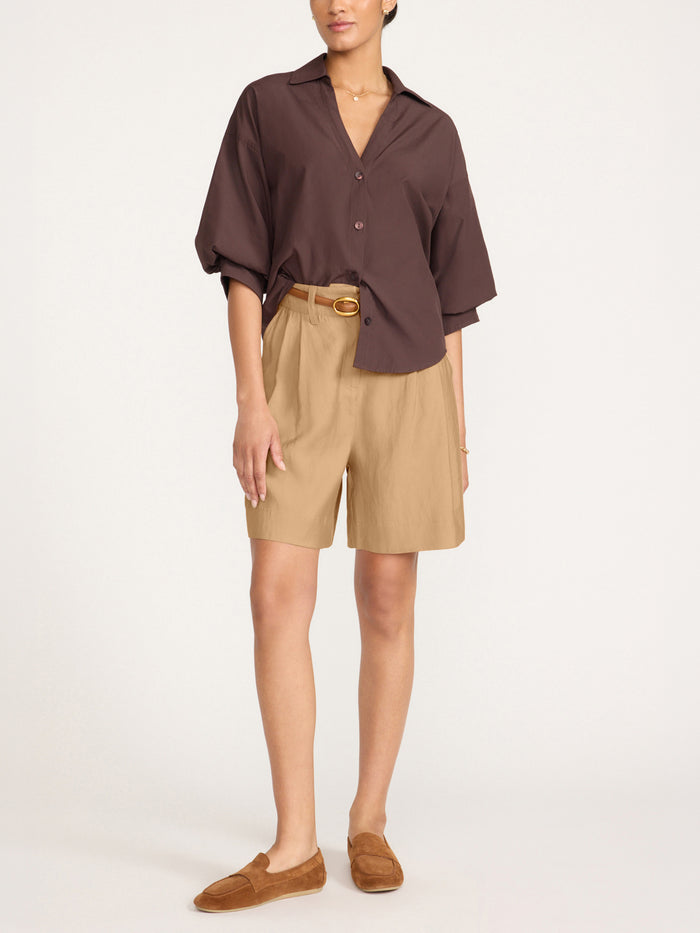 Woman wearing tan tailored shorts with a belted waist, styled with a brown blouse and loafers