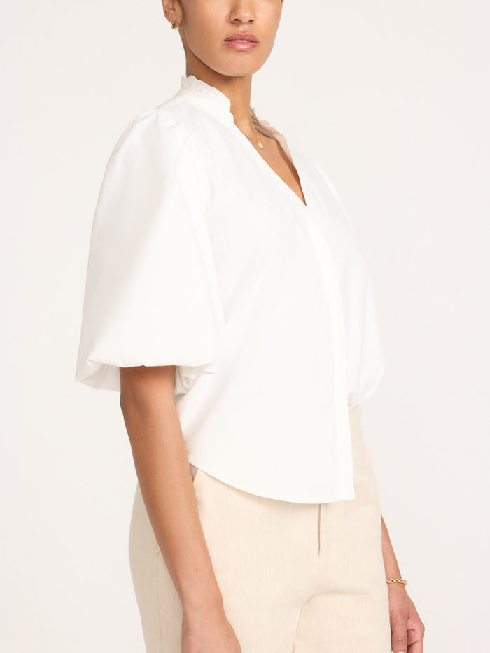 Side profile of the Marla Shirt in Salt White, a white puff-sleeve blouse with a stand collar, styled with beige trousers