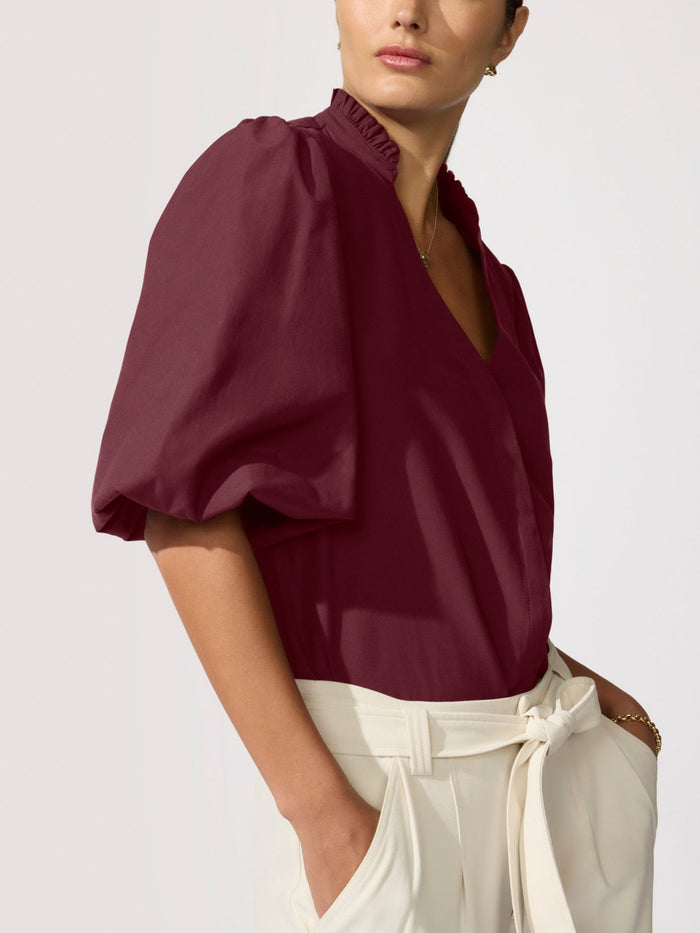 Close-up of a woman wearing a burgundy puff-sleeve blouse with a ruffled collar
