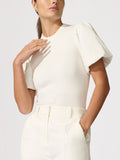 Close-up of a woman wearing an ivory puff-sleeve knit top with white trousers