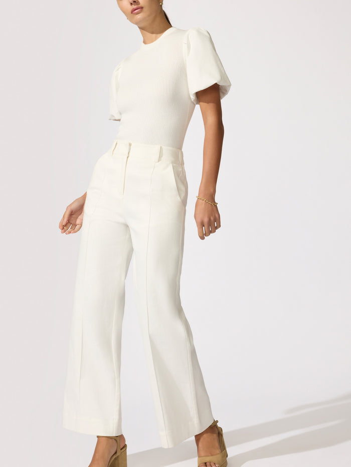 Woman wearing an ivory knit top with wide-leg white trousers and tan heeled sandals