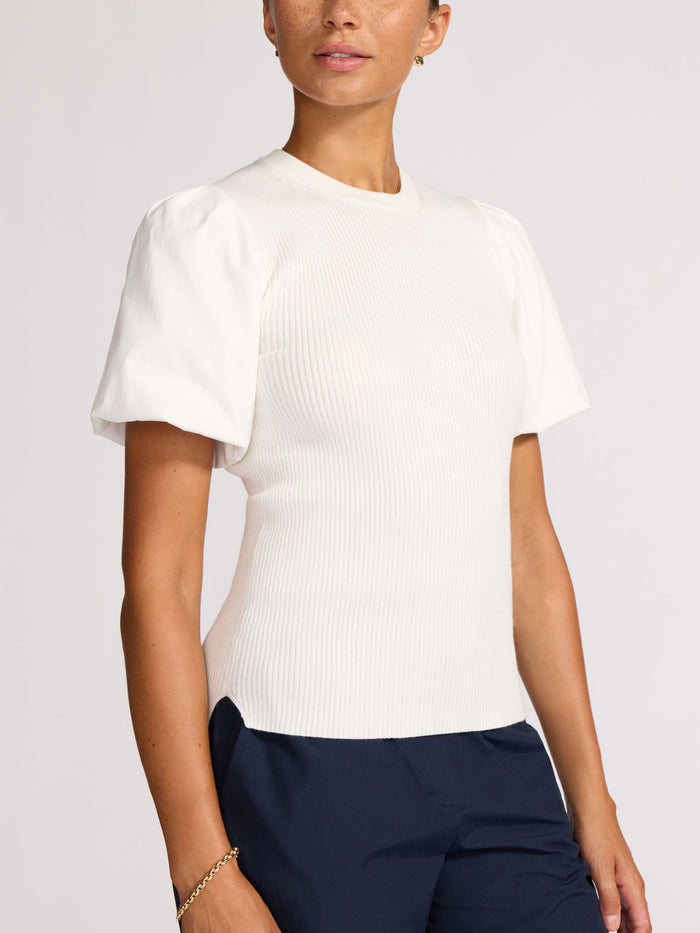 Front view of a woman wearing a white ribbed knit top with puff sleeves and navy trousers