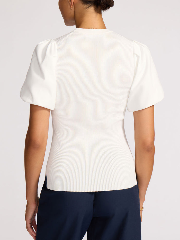 Back view of a woman wearing a white ribbed knit top with puff sleeves and navy trousers