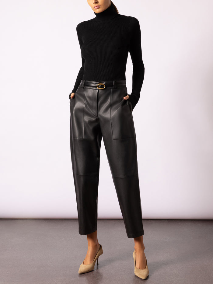 Full-length view of a model wearing black leather trousers with a black turtleneck and tan pumps
