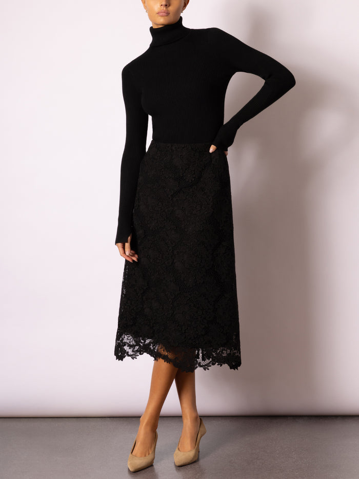 Full-length view of a model wearing a black turtleneck with a black lace midi skirt and tan pumps