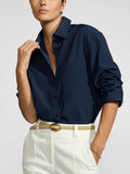 Model wearing the Pia shirt in navy tucked into white trousers with a tan leather belt