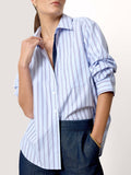 Close-up of a woman wearing a blue and white striped button-up shirt with rolled sleeves