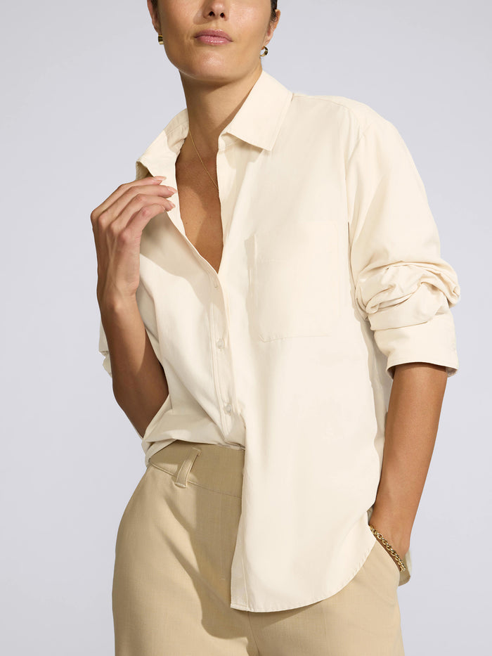 Model wearing a cream oversized button-down shirt with rolled sleeves and beige trousers
