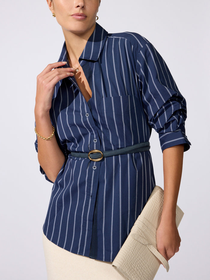 Pia shirt in Hartford stripe navy, model wearing belted button-down shirt with a cream clutch