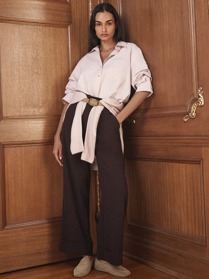 Model wearing a light pink button-up shirt with rolled sleeves and dark brown wide-leg trousers