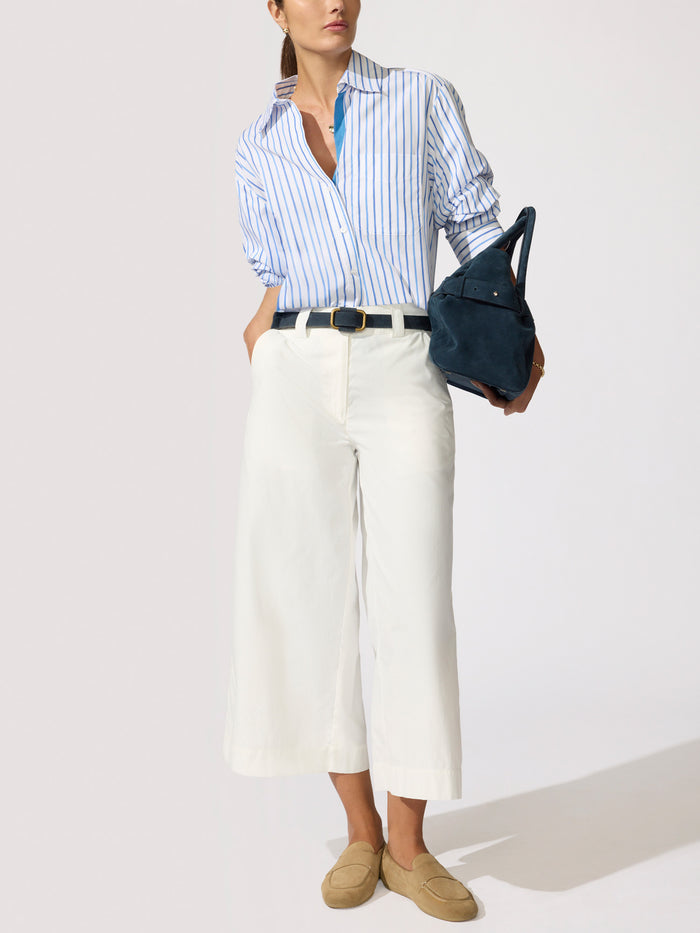 Woman wearing a blue and white striped button-down shirt with white wide-leg pants