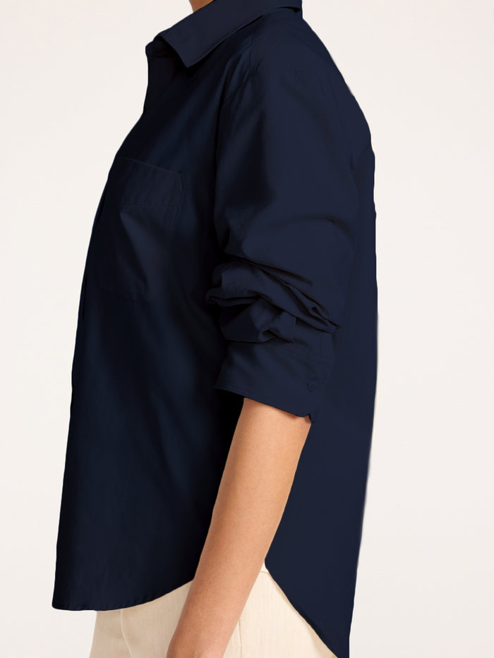 Button-down shirt in navy, close-up side view with rolled sleeves over beige pants