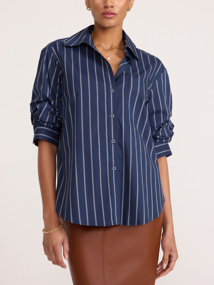 Woman wearing a navy button-up shirt with thin white pinstripes, tucked into a brown leather skirt.