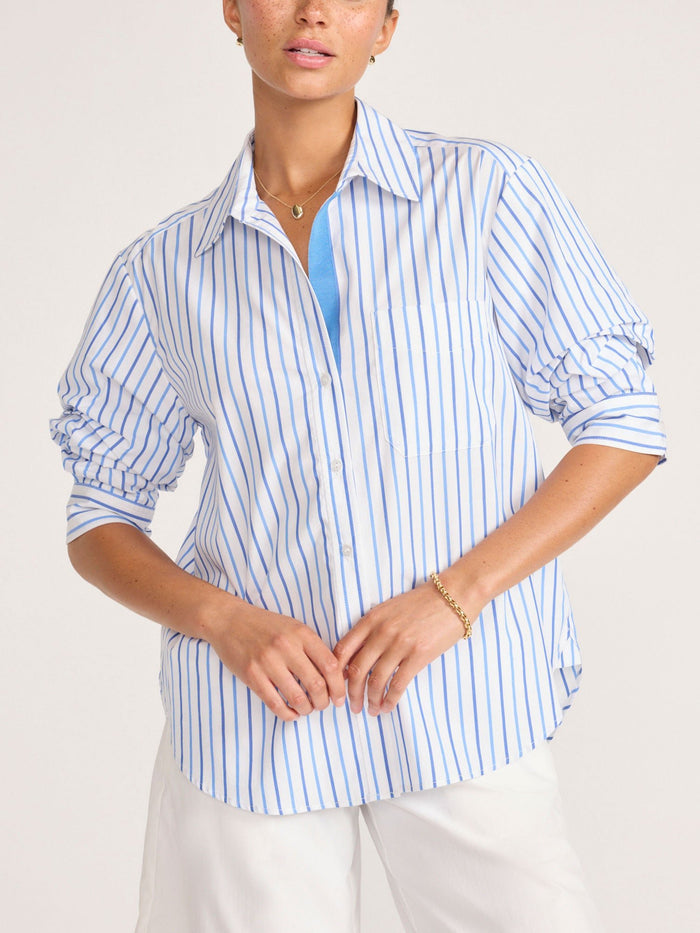 Model wearing a blue and white striped button-up shirt with white trousers
