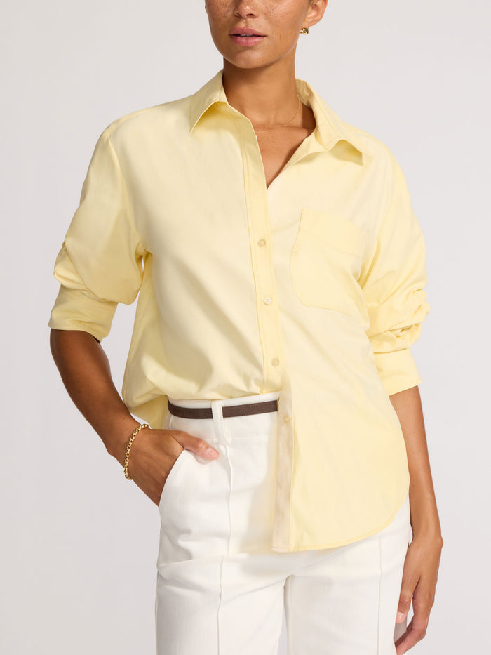 Front view of a model wearing a pale yellow button-down shirt with a chest pocket and belted cream trousers