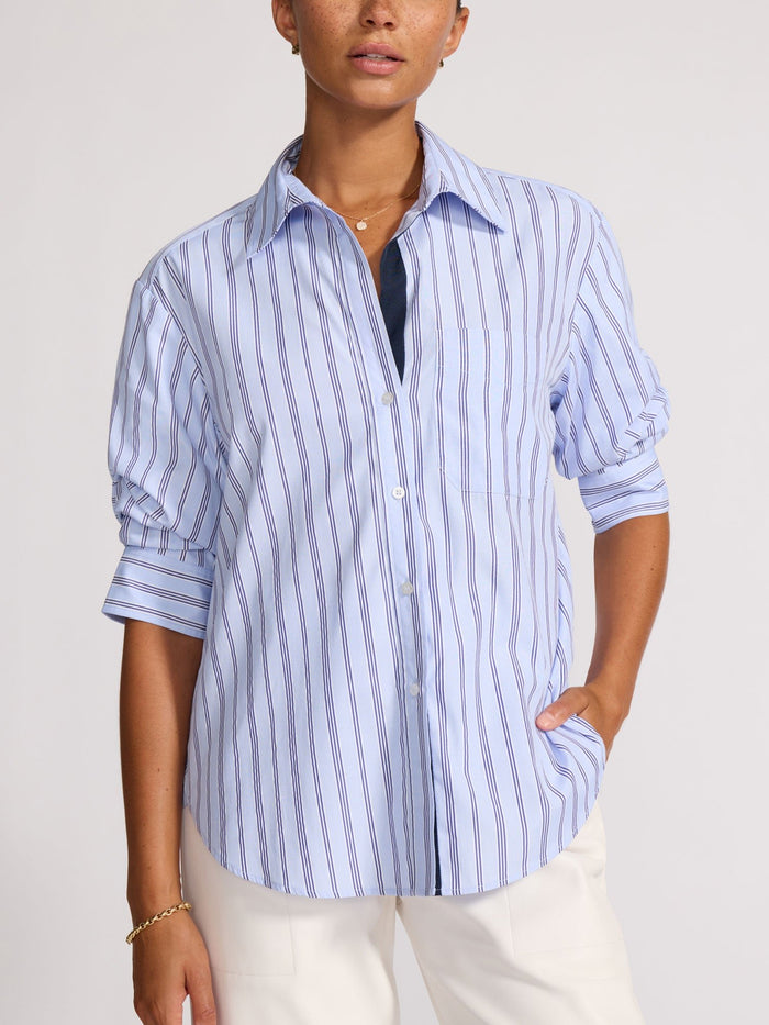 Front view of a model with hand in pocket wearing a blue striped shirt with rolled sleeves