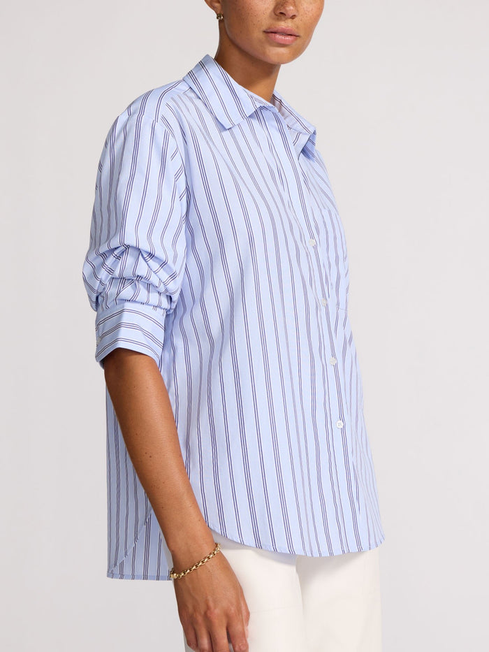 Side profile of a model wearing an oversized blue striped shirt untucked over white trousers