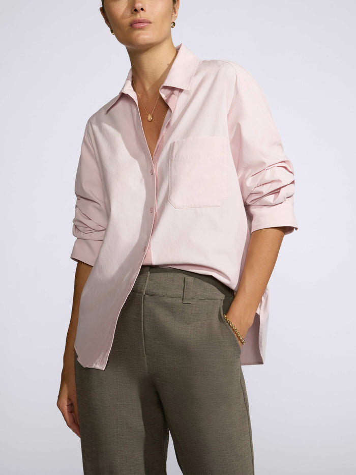 Close-up of a woman wearing a light pink button-down shirt with rolled sleeves and a chest pocket