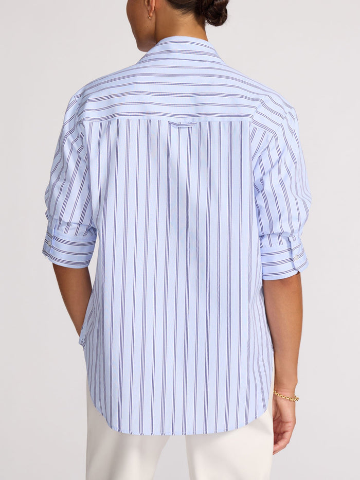 Back view of a model wearing a blue and white striped shirt with rolled sleeves and white trousers