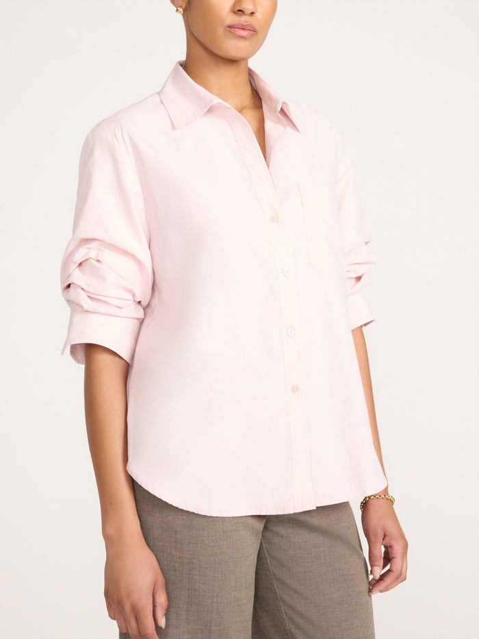 Woman modeling a blush pink button-up shirt with rolled sleeves and tailored gray trousers