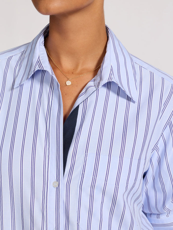Close-up of a model's neckline wearing an unbuttoned blue striped shirt with layered gold necklaces