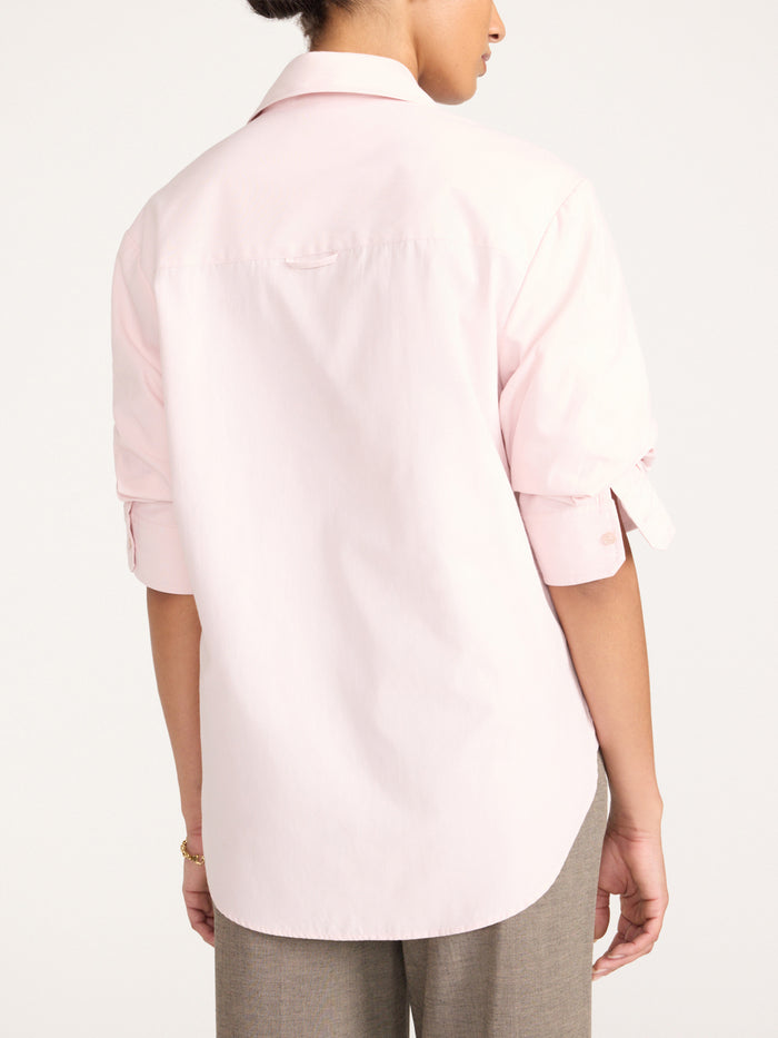 Back view of a woman wearing a pink button-up shirt with rolled sleeves and gray tailored trousers