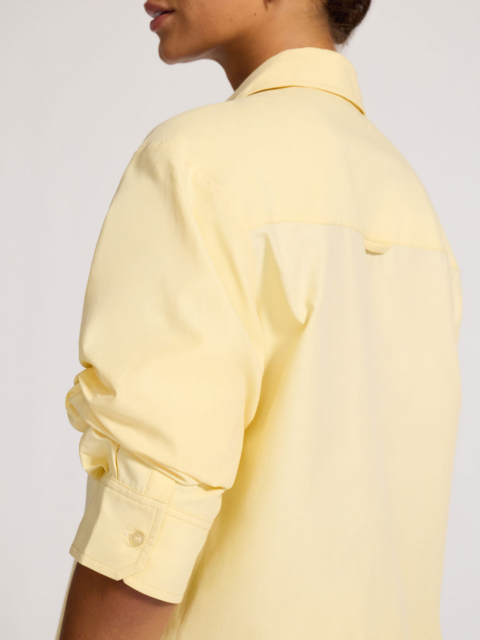 Close-up of the rolled cuff sleeve and shoulder seam on a pale yellow button-down shirt