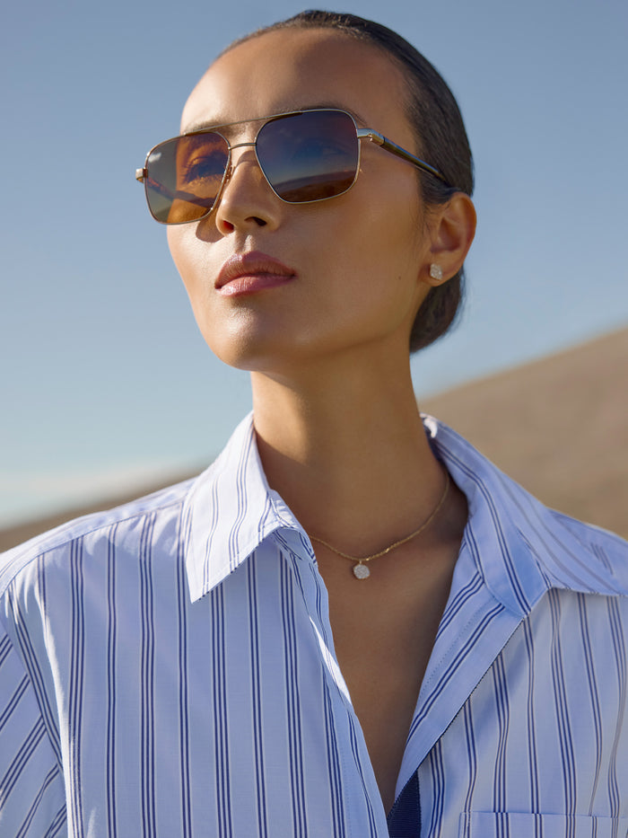 Woman wearing brown aviator sunglasses and a blue pinstripe button-down shirt outdoors