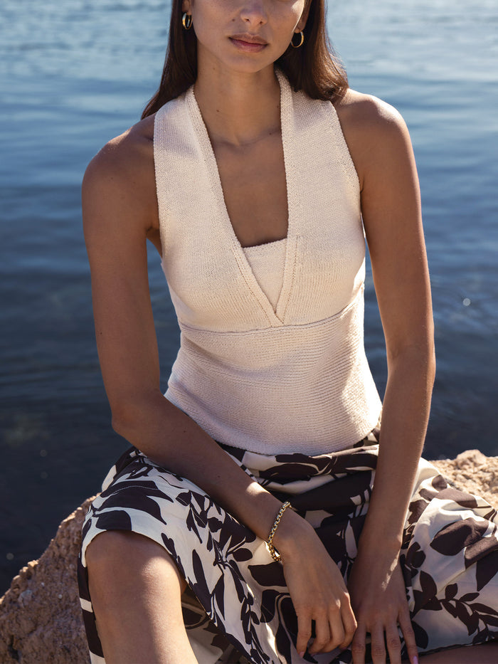Ribbed knit halter top in ecru, styled with a black-and-white floral skirt, seated by the water