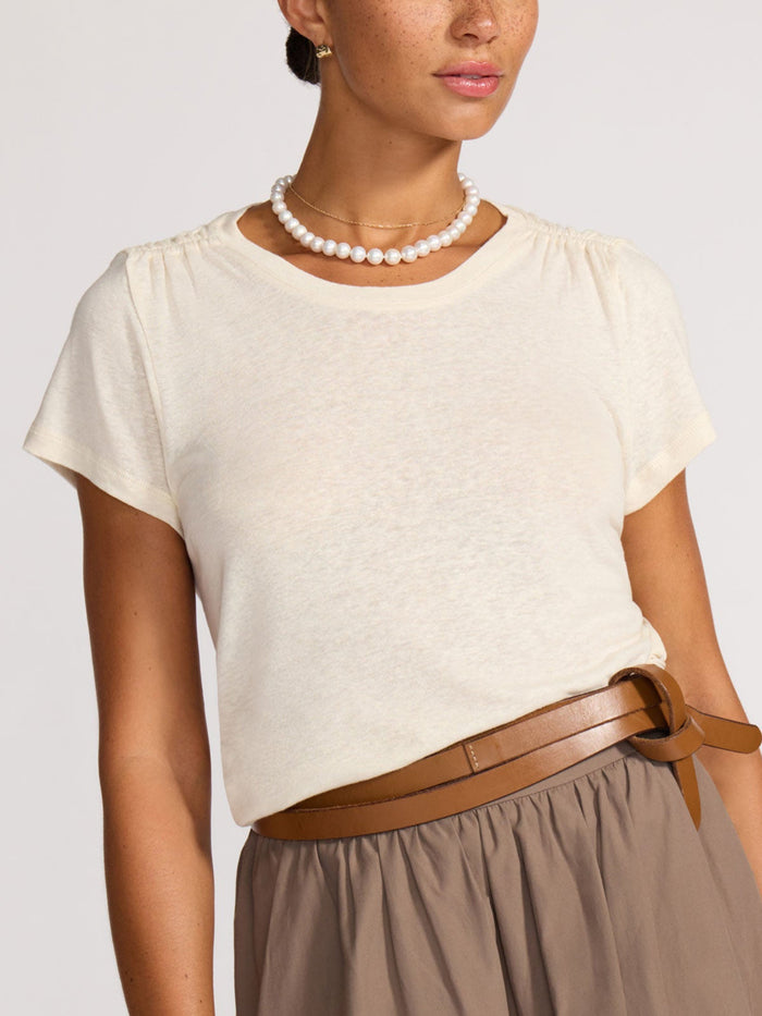 Close-up of a cream linen t-shirt with gathered shoulders, worn with a pearl necklace and gold chain.