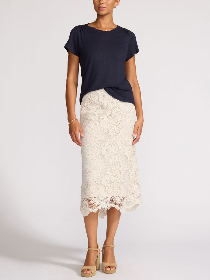 Woman wearing a navy t-shirt with a cream lace midi skirt and tan block-heel sandals.