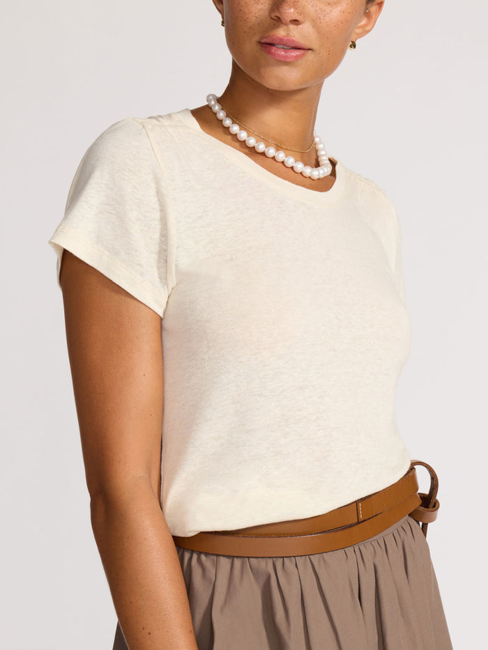Close-up of a cream linen t-shirt tucked into a taupe skirt with a brown leather belt and pearl necklace.