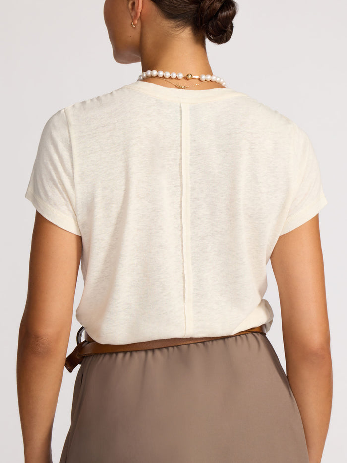 Back view of a cream linen t-shirt tucked into a taupe skirt with a brown leather belt.