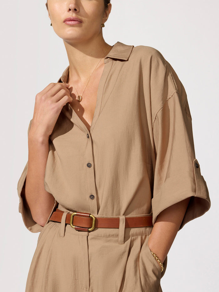 Close-up of a woman wearing a tan button-up shirt cinched with a brown leather belt
